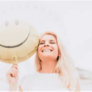 woman smiling holding smiley face balloon